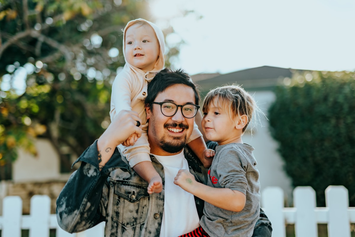 A parent smiling while holding two children outdoors